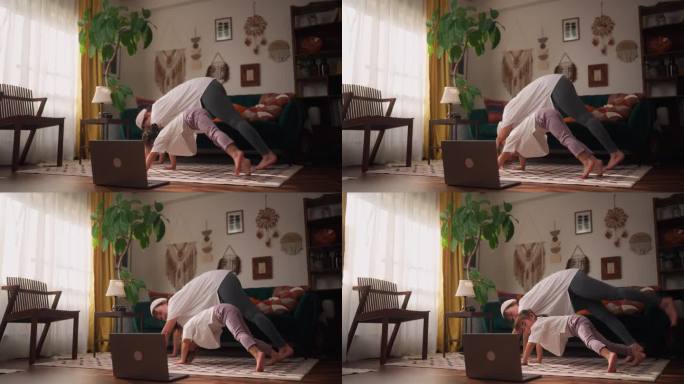 母亲用笔记本电脑观看在线瑜伽课程，在家里的客厅和小女儿一起练习