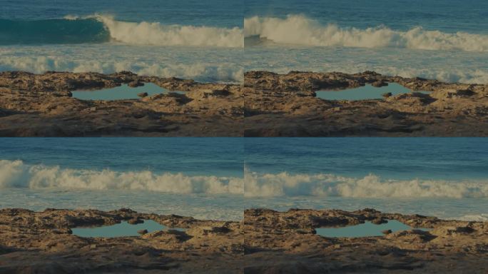 在夏威夷瓦胡岛的海滩上，一个波浪在蓝绿色的太平洋水域中达到完美的滚动，前景是一个潮汐池