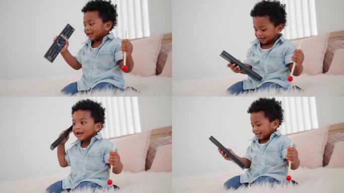 一个穿着休闲装的14个月大的小男孩在家里用电视遥控器给妈妈拨电话。非洲小孩坐在家里的毛绒地毯上，把电