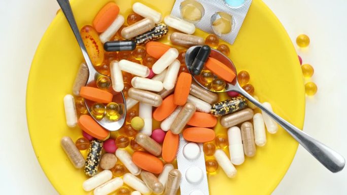旋转的黄色盘子里盛满了药品和补品，健康理念，过量食用的药品和补品，平铺，白色背景
