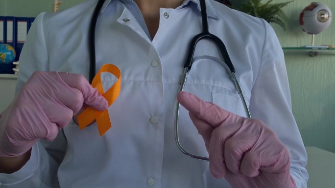 医生拿着橙色的白血病、癌症、多发性硬化症和多动症的宣传丝带
