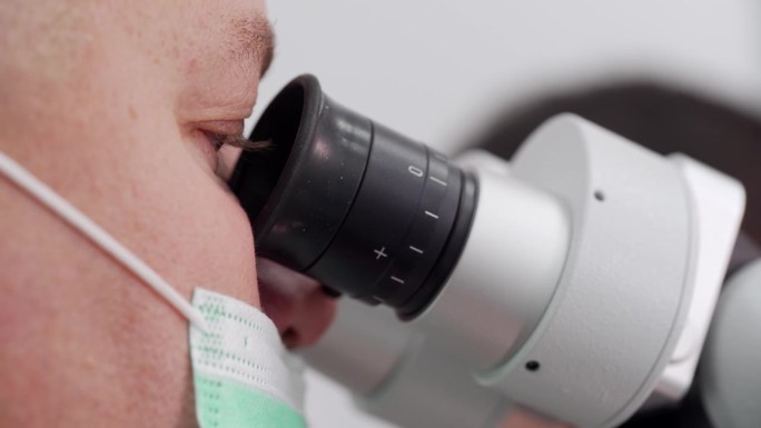 男科学家戴着医用口罩，在生物技术实验室里观察显微镜的特写。病毒学家在显微镜下分析疫苗样本。科学家在实