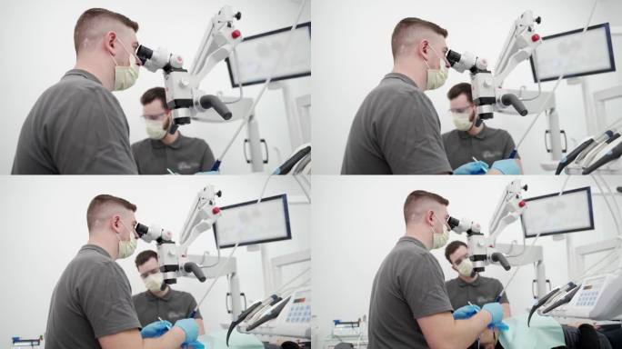 现代牙科诊所，男牙医与助手用显微镜操作病人牙齿。医生清理牙根管，烧灼牙神经。牙髓医生治疗病人的根管。