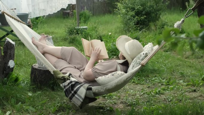 一位女士沉浸在文学和自然的双重疗法中，在花园的吊床上平静地阅读，心理健康成为人们关注的焦点。自我照顾