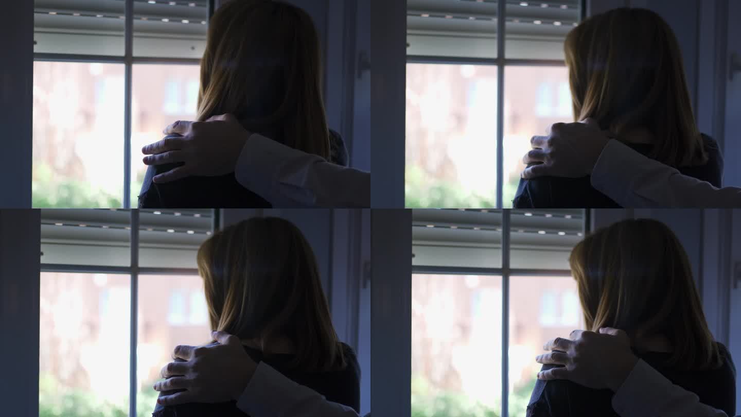 一个男人的手搭在一个沮丧的女人的肩膀上，她看着窗外
