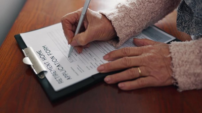 老年妇女，手写着退休申请表，遗嘱或养老合同放在桌上。老年女性为房屋或契约签署或填写文件或法律政策的特