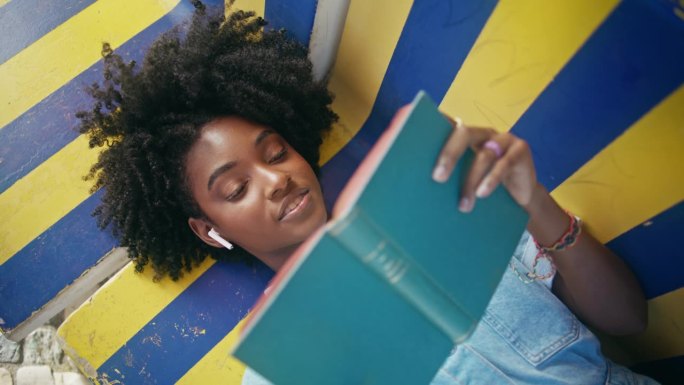 青少年躺在户外长凳上大声朗读。女孩喜欢文学