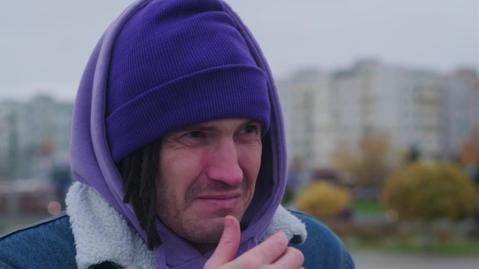 一名男子站在城市街道上，在寒冷的天气里抽泣。冻僵的人穿着暖和的衣服，流着鼻涕，擦着鼻子。