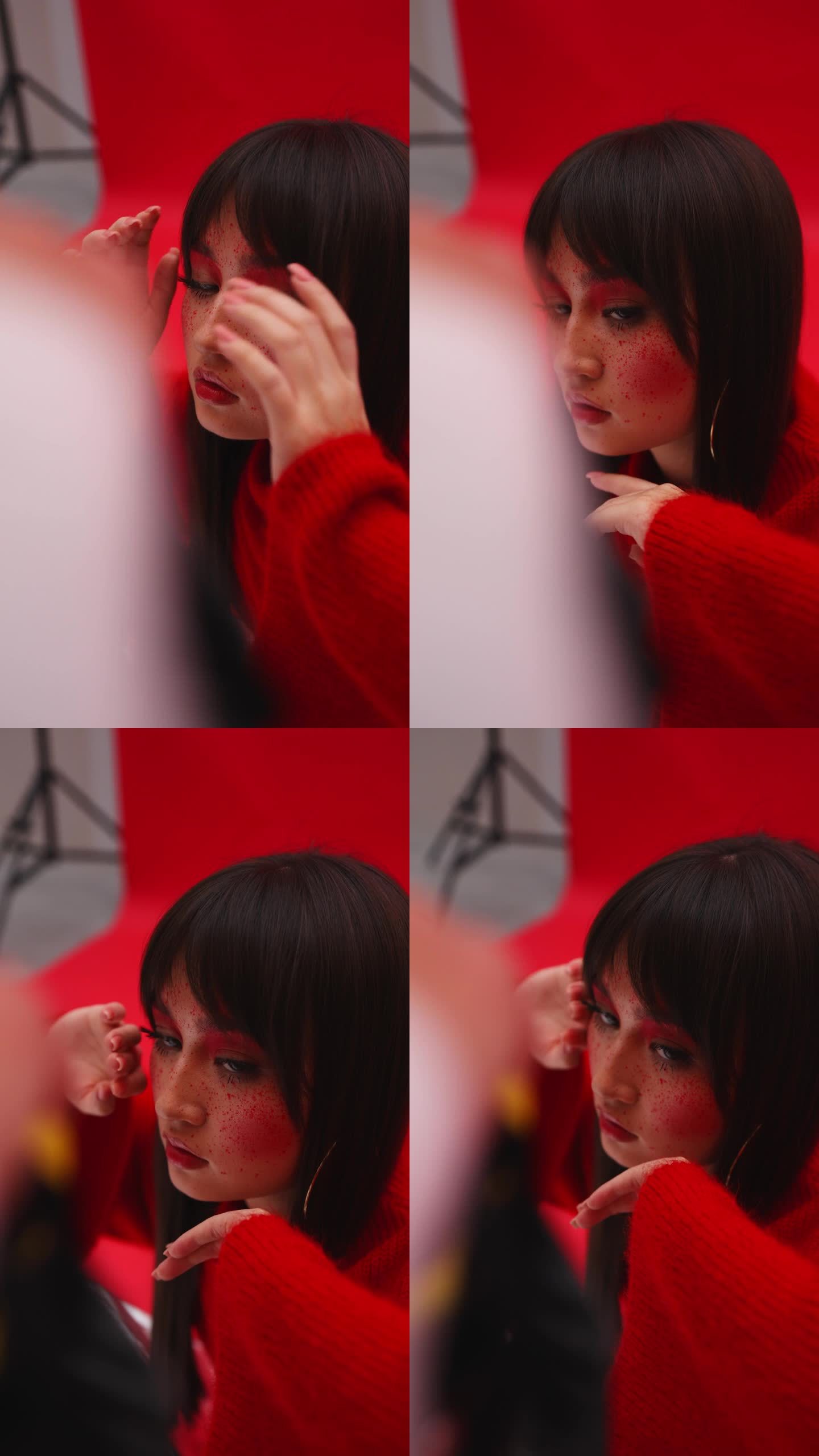 一个亚洲女孩在摄影棚的摄影师面前摆姿势。特写红色背景。相机闪光。垂直视频