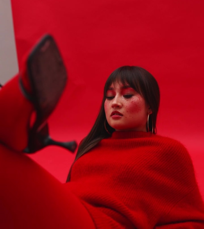 亚洲模特女孩躺在地板上的红色背景，穿着红色毛衣和连裤袜。脚对脚穿高跟鞋。艺妓穿着红色的衣服。相机旋转