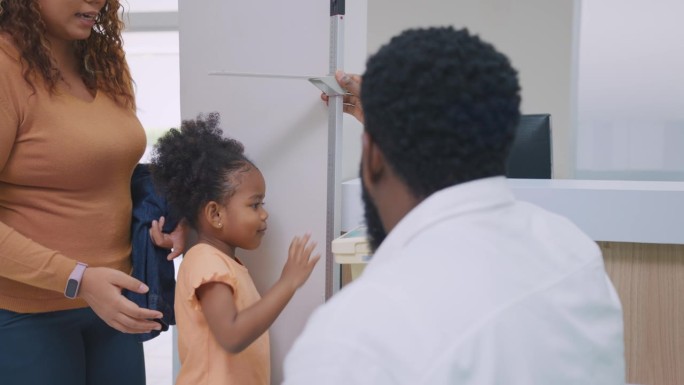 有魅力的父母在医院里测量非洲小女孩的身高。在卫生所的走廊里预约时，漂亮的一家人心情愉快地准备着医生的