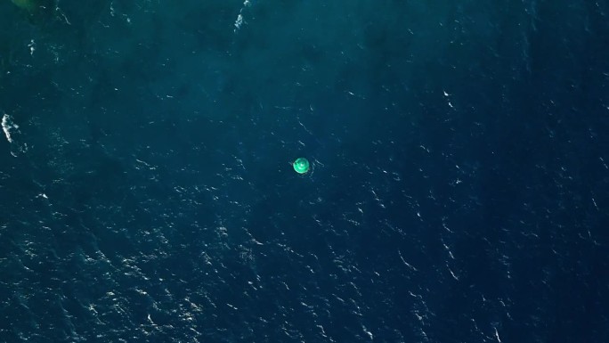 航拍无人机在开阔的绿蓝色梯度海水中俯首向下的浮标