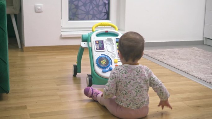 一个可爱的小女孩在家里玩玩具学步车