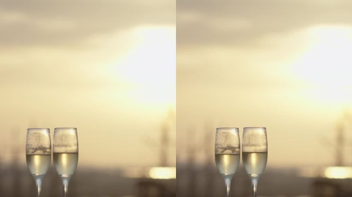 垂直视频。浪漫的夜晚，阳台上的两杯香槟。背景是明亮的夕阳和老船的高桅杆。