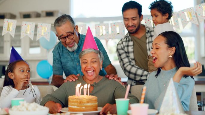 生日，聚会和一位老妇人与她的家人在家里一起庆祝一个人生里程碑事件。孩子们，父母和祖父母在家里吃蛋糕庆