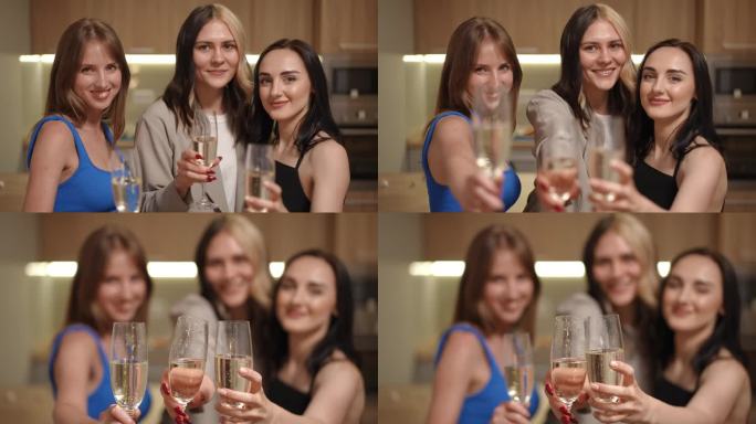 三个女孩站在一间现代公寓的厨房里，手里拿着几杯白起泡酒。女孩们对着镜头拿出笛子，喝着酒，微笑着看着镜