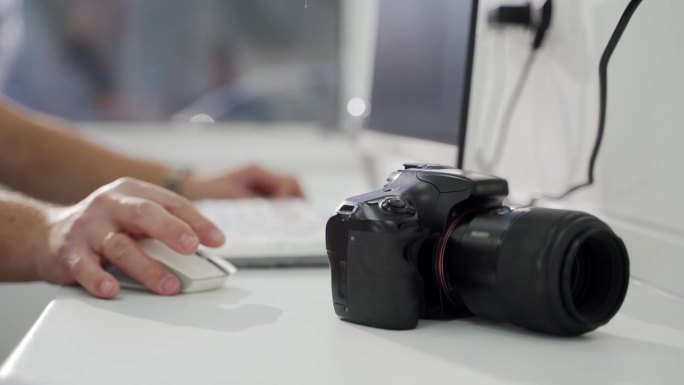 桌子上的专业黑色相机，摄影师的手在电脑上工作，在办公室上传照片。现代摄影设备。将照片从相机传输到电脑