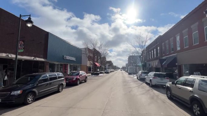 汽车视角拍摄:在一个晴朗的日子里，天空中有云，在一条主要道路上开车经过奥尔温的小镇商业