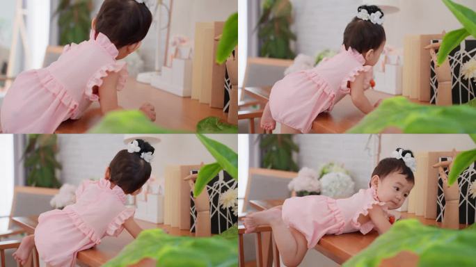 可爱的亚洲女婴穿着可爱的粉色连衣裙，爬上她家客厅的高桌上，试图够到东西。