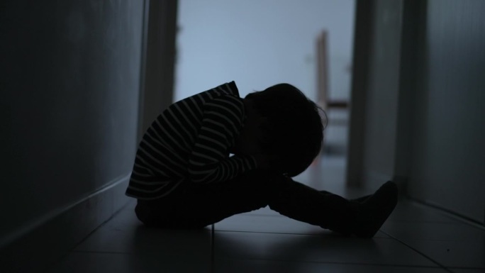 一个害怕绝望的孩子坐在家里黑暗的走廊里捂着脸。童年的孤独和绝望的概念