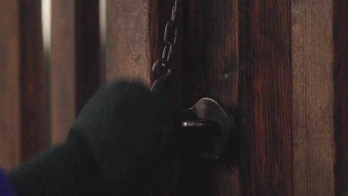 一只手从旧木门的锁上拔出旧门闩的特写