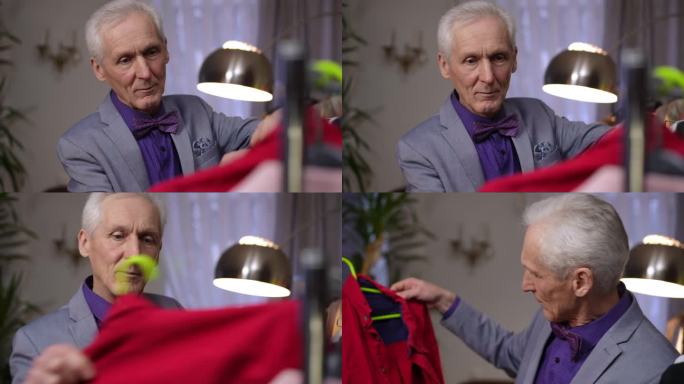 特写镜头。一位头发花白的老年男性时装设计师正在检查和挑选挂在移动衣架上的衣服。