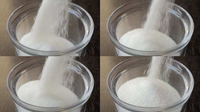 在糖碗里倒糖慢动作。一堆白糖落在玻璃陶器里的慢动作。不健康饮食的概念，糖尿病，肥胖，心脏病。甜食上瘾