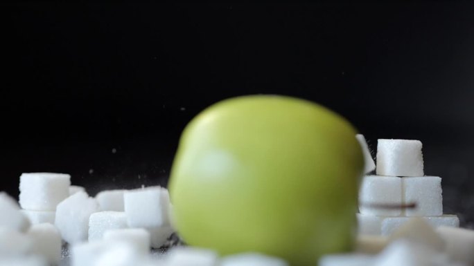 慢动作绿苹果冲破白糖方块堆积的墙。选择健康的生活方式。不健康饮食的概念，糖尿病，肥胖，心脏病。甜食上