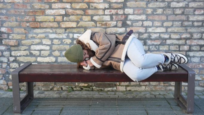 无家可归的小女孩睡在街上的长椅上。女性因天气寒冷在公交车站或火车站等车迟到。无家可归和被遗弃的青少年