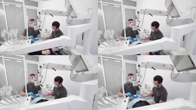 现代牙科诊所男牙医与助手用显微镜操作病人牙齿。口腔外科医生清洁牙根管并烧灼牙神经。牙髓医生治疗病人的