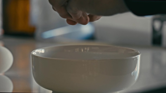 双手打开生鸡蛋放入白碗中做早餐。