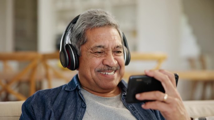 笑着，老人和手机上的视频，在网上看电影或电影。快乐，流媒体，一个戴着耳机的老人，手机和家里沙发上的一