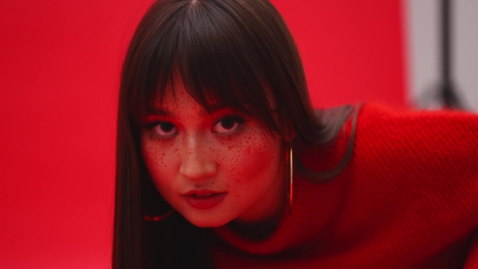 一个亚洲女孩的特写，红色背景，脸上有雀斑。艺伎在摄影棚里摆姿势