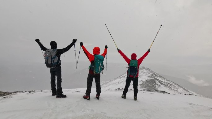 图为，登山队员们站在高海拔的山顶上，举着手欣赏风景。
