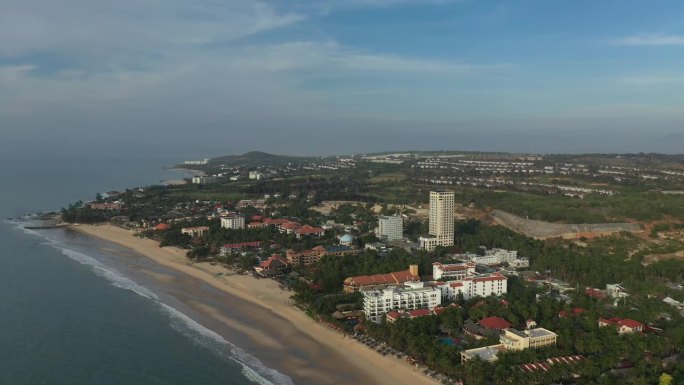 清晨，在金色的阳光下，越南梅尼度假胜地的空中轨道照片，有游泳池、海滩、建筑和花园。越南著名的度假小镇