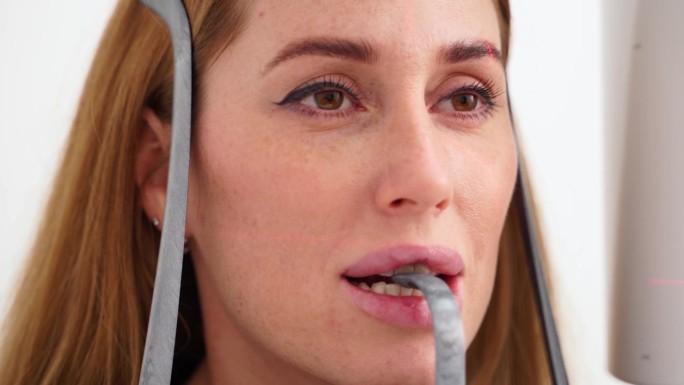 头部全景x光机拍摄的女性脸部特写。女病人站在牙科x光机前进行牙科x光摄影。拍下巴全景的女人。