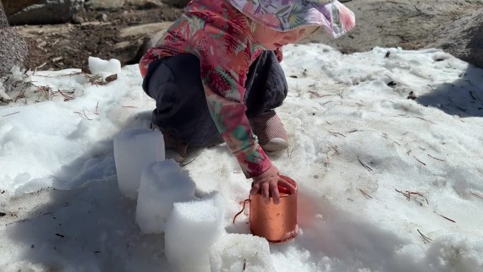 初学走路的孩子在春天的雪地里拿着杯子玩耍