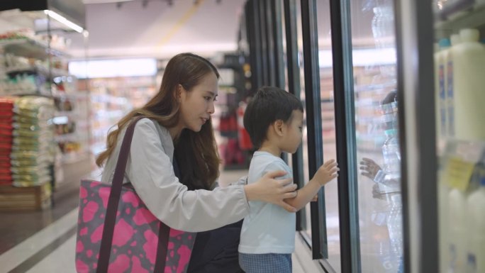 年轻漂亮的亚洲护士穿着工作服和她的儿子在医院下班后一起去购物中心的超市买食物。