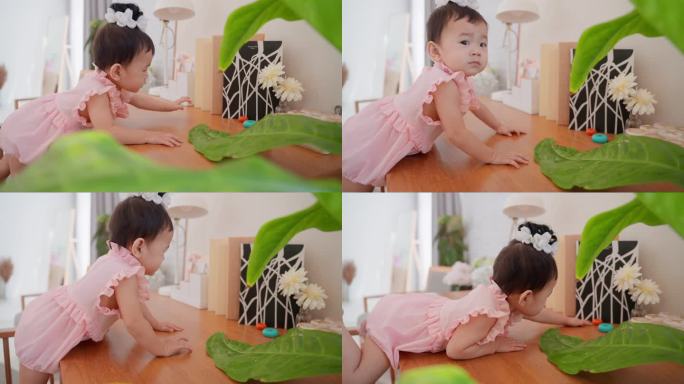 可爱的亚洲女婴穿着可爱的粉色连衣裙，努力爬上妈妈的工作台，去够她家客厅里的东西