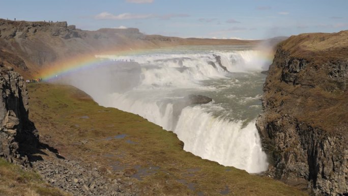 在冰岛晴朗的天空下，雄伟的瀑布和充满活力的彩虹穿过岩石地形
