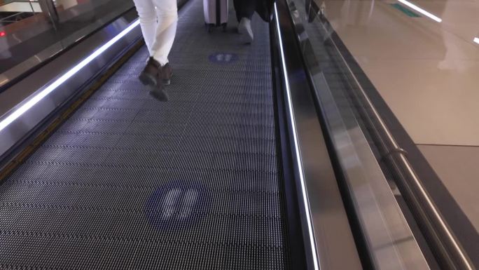 在机场，乘客提着行李箱走在移动通道上。
