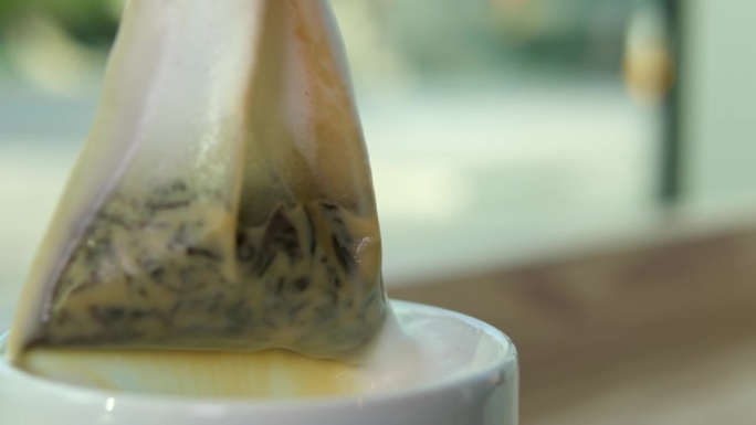 奶茶，一袋袋草本绿茶从白色的杯中提起，美味的饮品流到桌上，奶沫、鲜奶油的近景，利于感冒、暖身、饮热腾