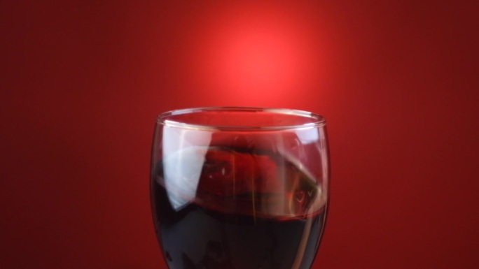 暖色调的灯光下，在暗色背景墙上摇曳着酒杯里的红酒。美丽的葡萄酒商业素材。高脚杯内的调酒过程特写。慢动