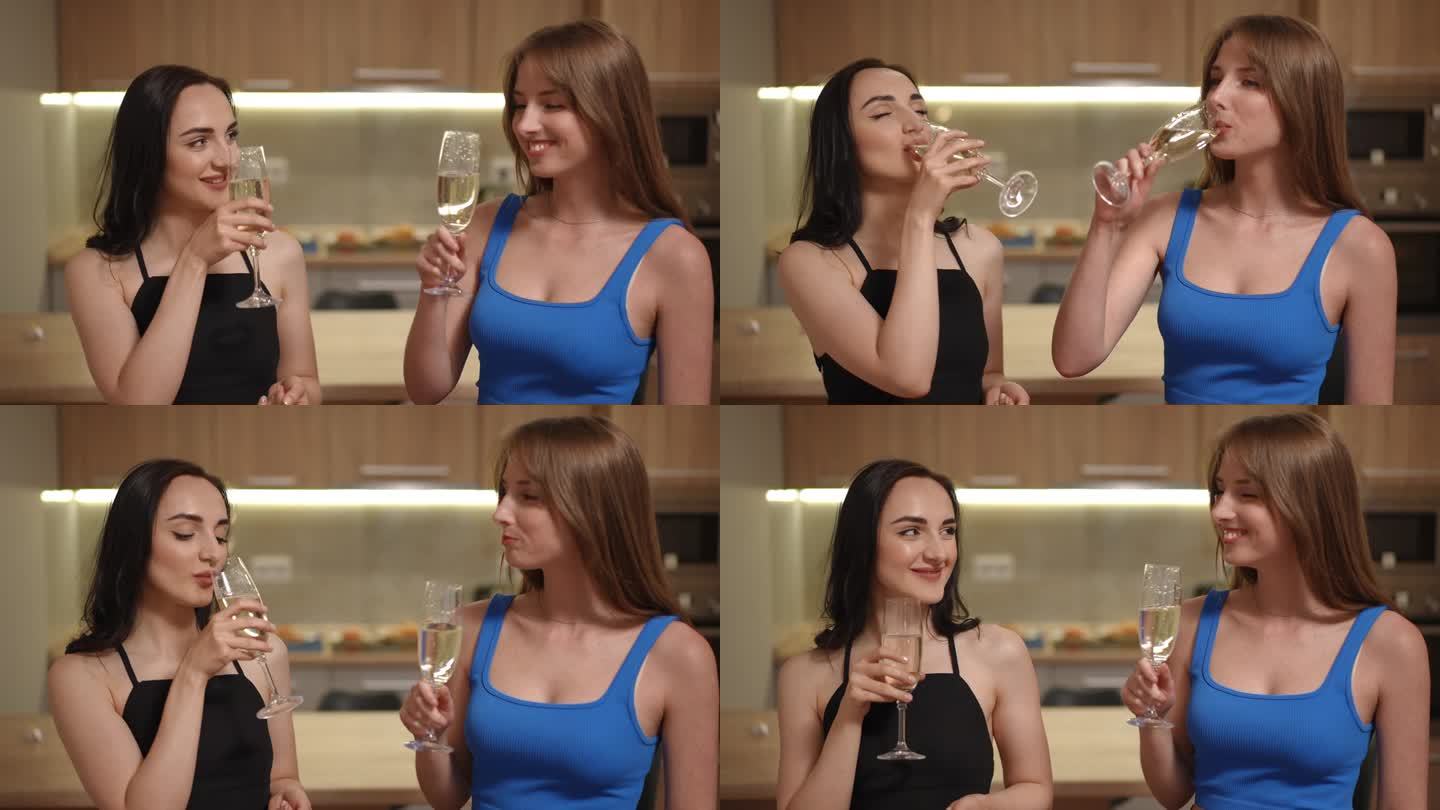两个女孩站在公寓里的现代厨房里，用白葡萄酒碰杯。女孩们拿着杯子喝酒，面面相觑。看着镜头微笑的年轻女性
