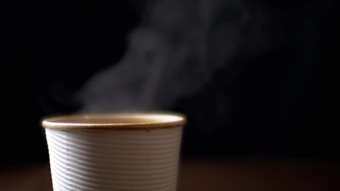 近距离观察，黑色背景上，热咖啡从纸杯里冒出来的热气