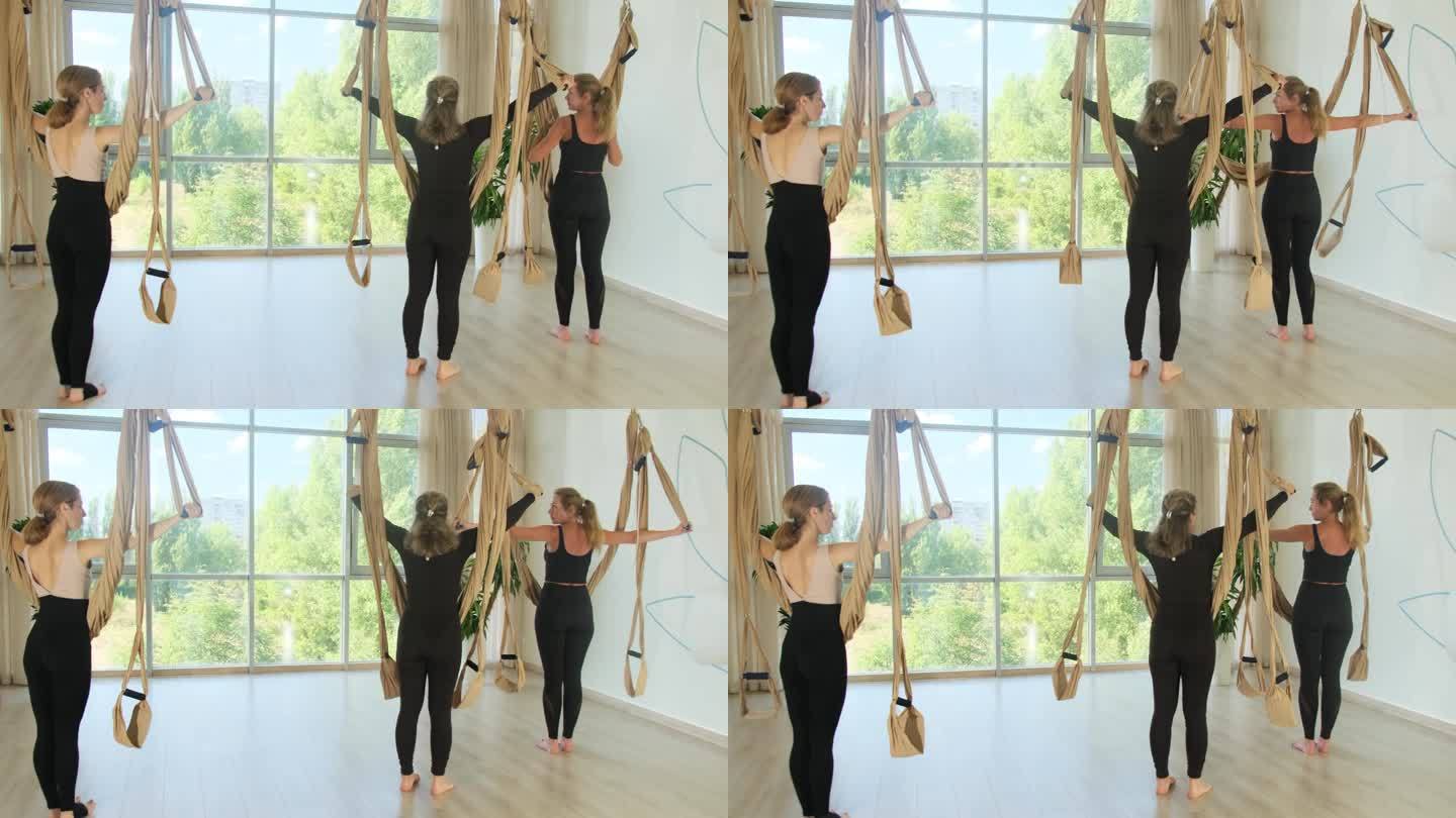 女学员在健身房与教练一起进行空中瑜伽练习