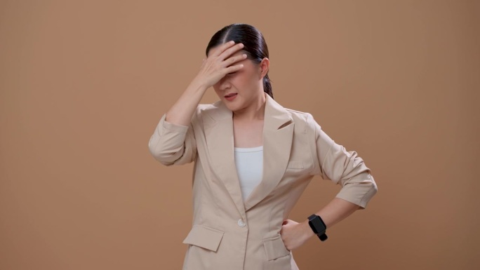 一名亚洲妇女患头痛，独自站在米色背景上。