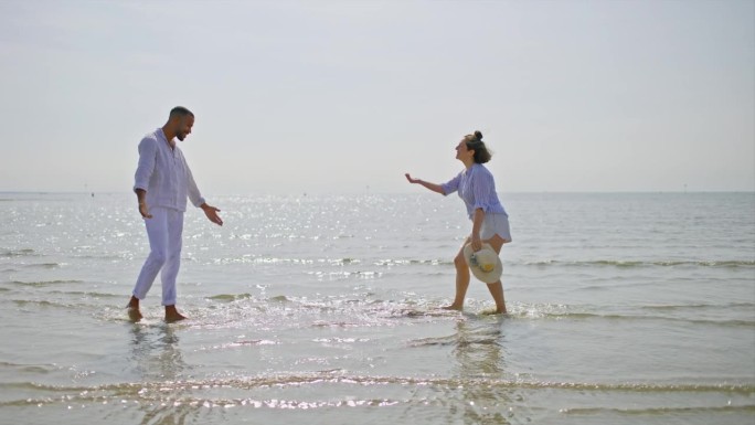 一对夫妇在阳光明媚的海滩上赤脚在水里跑步