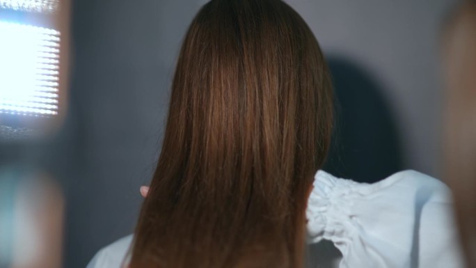 在一家现代美发沙龙里，理发师用吹风机吹干一个女孩的头发后，用手摇着她的头发。特写，后视图。