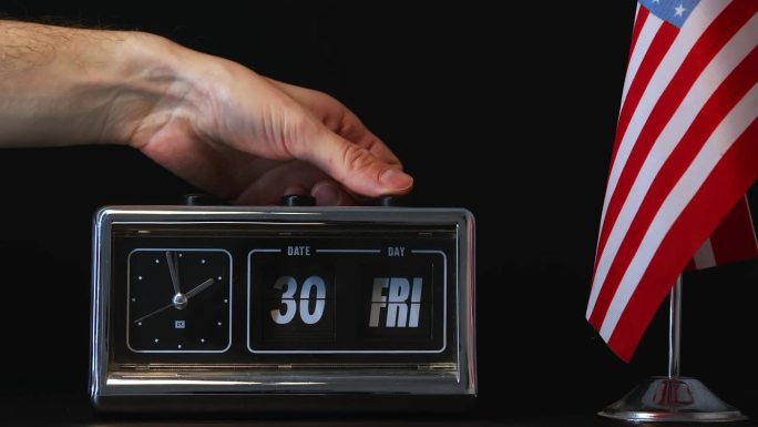 手动调整一个老式翻盖时钟，显示第30天，并有一面美国国旗，代表准时日期跟踪在美国文化和商业中的重要性